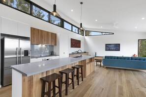 A modern kitchen with a large island, wooden cabinets, and a blue sofa in the living area.