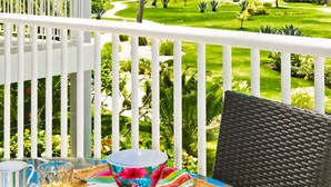 Un balcon avec une table dressée pour le petit-déjeuner, donnant sur un jardin bien entretenu et une piscine.
