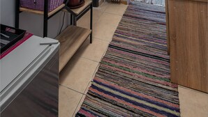 A compact hotel room with a kitchenette, a bed with a view, a small table, and a colorful striped rug. - Tonia's house in Athens (Athens)