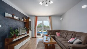 Una sala de estar moderna con un sofá de cuero marrón, una mesa de centro de madera, un televisor de pantalla plana sobre un mueble de madera y un amplio ventanal con vistas a una piscina y zonas verdes.