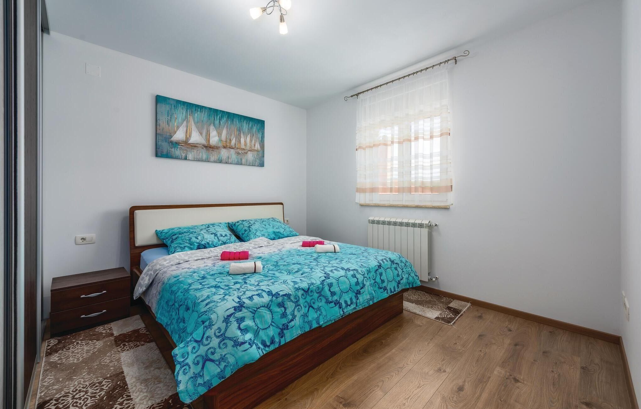 A bedroom with a bed, a nightstand, a dresser, a painting, a window with curtains, and a radiator.