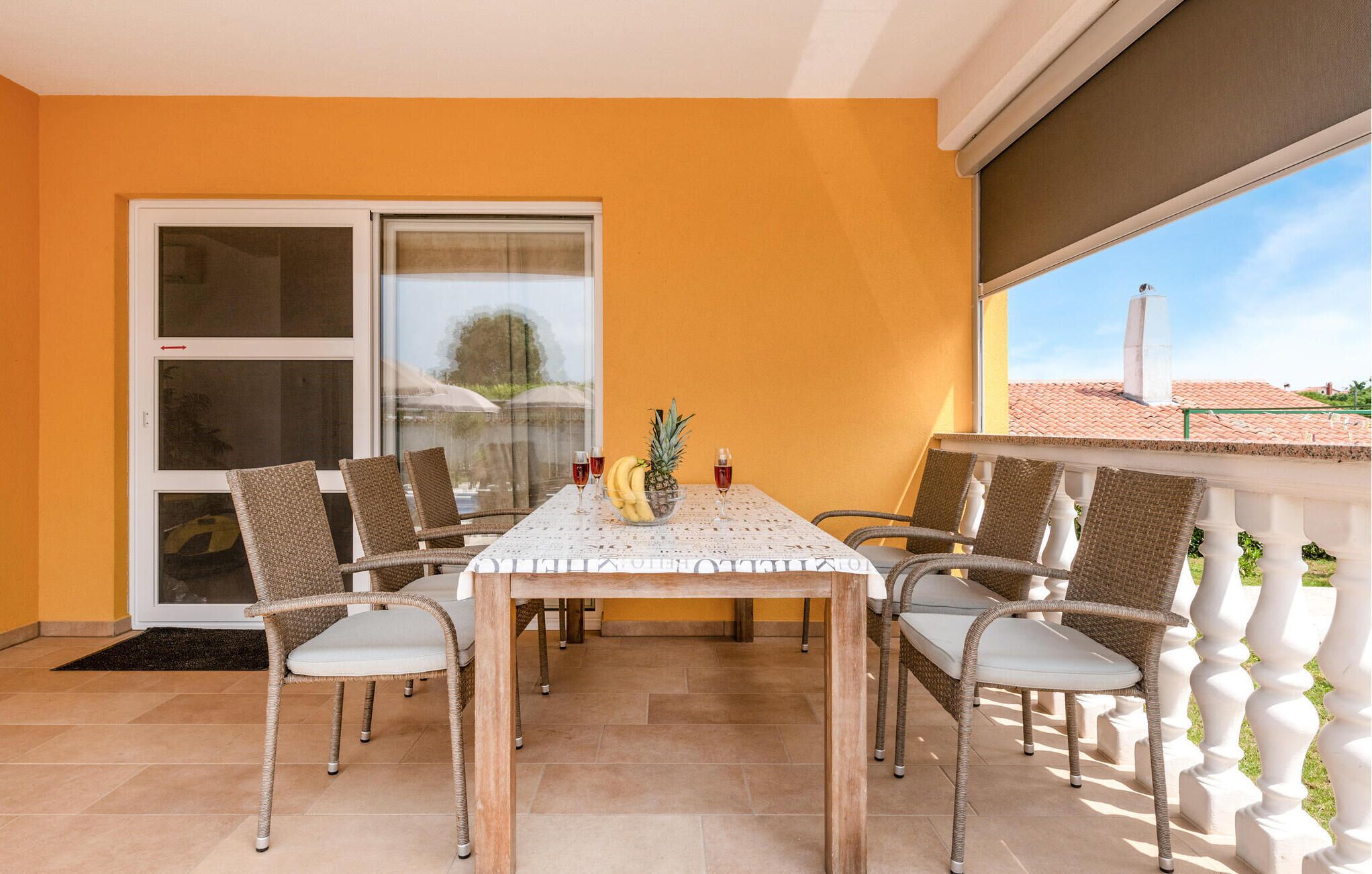 A dining area with a table set for four, surrounded by wicker chairs, a glass window, and a view of a red-tiled roof.