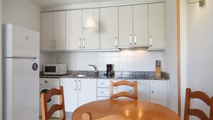Een compacte keuken met witte kastjes, een magnetron, een koffiezetapparaat en een spoelbak. Er staat een rond houten tafel met vier stoelen.