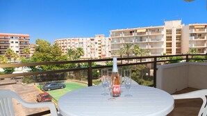 Een balkon met een ronde tafel, witte plastic stoelen en een fles wijn.