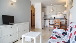 Een ruimtelijk ingerichte leefruimte met een kitchenette, een eethoek en een bank.