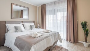 A neatly made bed with pillows, a bedside table with a lamp, and a large window with curtains. - VILLA NICOLINA - AP MARIELLA PRIVATE SUN DECK WITH JACUZZI (Kaštel Novi)