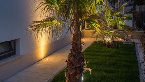 A modern building with a well-maintained lawn and a palm tree in the foreground. - VILLA NICOLINA - AP MARIELLA PRIVATE SUN DECK WITH JACUZZI (Kaštel Novi)