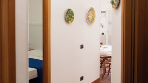 Um corredor estreito com soalho em azulejos, portas de madeira e duas placas decorativas nas paredes.