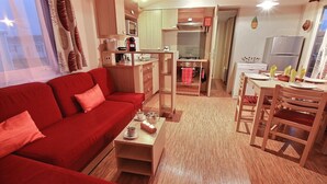 Ein kompakter Wohnbereich mit einem roten Sofa, einem Couchtisch, einem Essbereich mit Tisch und Stühlen, einer Küchenzeile mit Herd und Mikrowelle sowie einer kleinen Küche mit Kühlschrank.