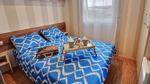 Ein Schlafzimmer mit Bett, Nachttisch, Koffer und Fenster.