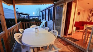 Eine überdachte Terrasse mit einem runden Tisch und Stühlen, eine Glasschiebetür zu einem Innenraum mit einem roten Sofa und einem kleinen Tisch.