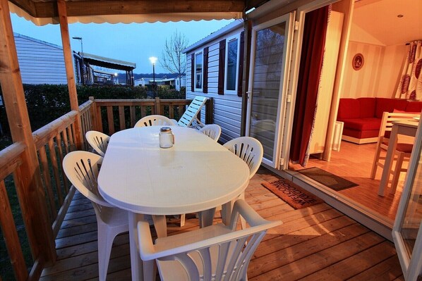 A covered outdoor deck with a round table and chairs, a sliding glass door leading to an interior room with a red couch and a small table.