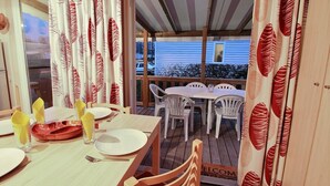 Ein Essbereich mit einem für vier Personen gedeckten Tisch, weißen Stühlen und einem roten und weißen Vorhang mit Blattmuster.