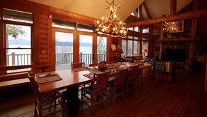 A wooden cabin interior with a dining table, chairs, a chandelier, and a fireplace. - Sunset Cabin - Flathead Lake, Exquisite Log Home and Guest Cabin. Sleeps 12 (Bigfork)