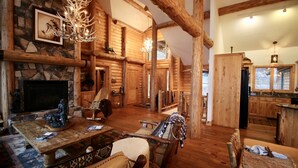 A log cabin interior with a stone fireplace, wooden furniture, and a chandelier. - Sunset Cabin - Flathead Lake, Exquisite Log Home and Guest Cabin. Sleeps 12 (Bigfork)