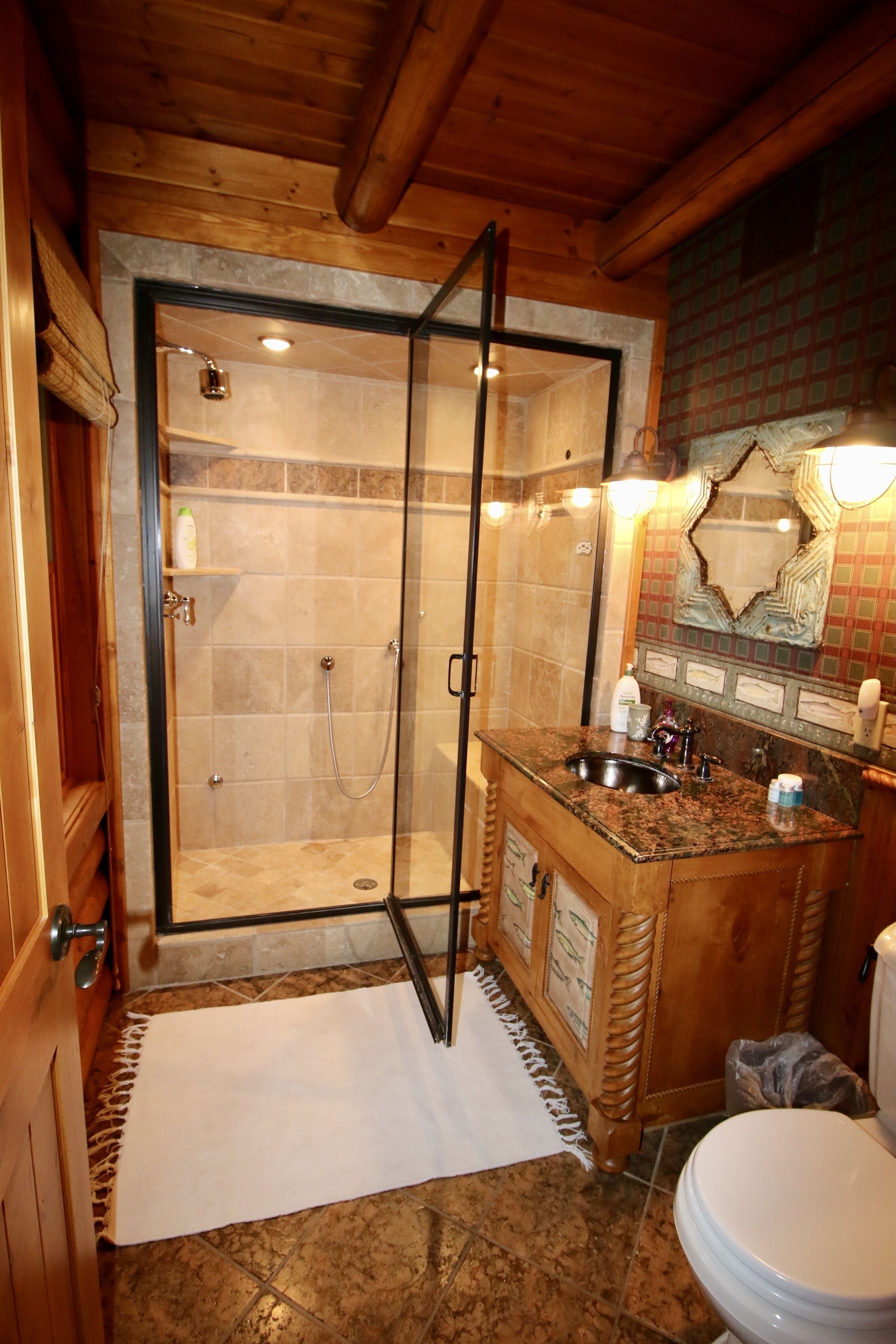 A wooden cabin bathroom with a glass-enclosed shower, a marble sink, and a toilet.