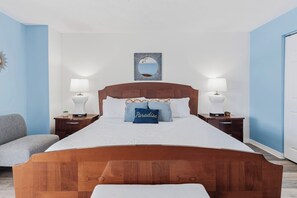 A bedroom with a wooden bed, two bedside tables with lamps, a wall-mounted mirror, and a blue accent pillow.