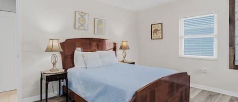 A bedroom with a wooden bed, two bedside tables with lamps, a ceiling fan, and a window with blinds.