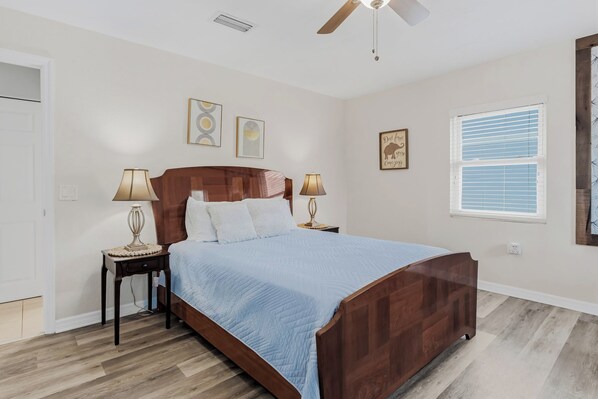 Un dormitorio con una cama de madera, dos mesitas de noche con lámparas, un ventilador de techo y una ventana con persianas.