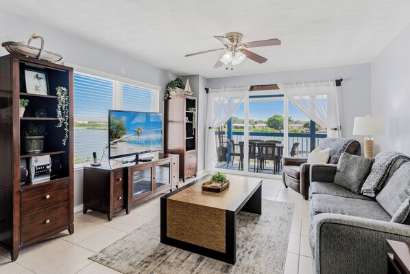 A living room with a television, a sofa, a coffee table, and a view of a body of water through large windows.