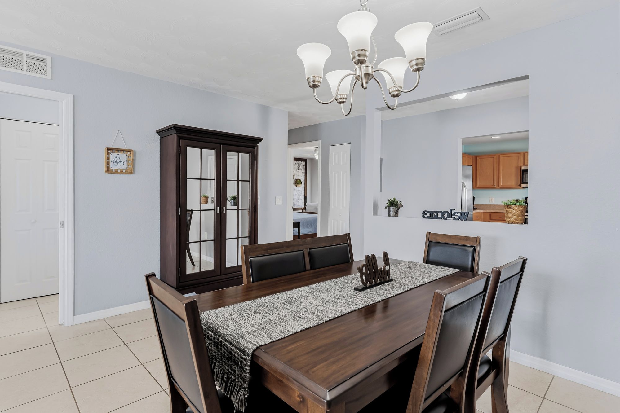 A dining area with a wooden table, chairs, a chandelier, and a cabinet with glass doors.
