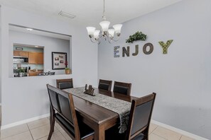 A dining area with a wooden table and chairs, a chandelier, and a kitchen visible through an open door. - Caddy's Boat House – Waterfront Balcony, Pet-Friendly & Steps from Indian Shores Beach (Indian Shores)