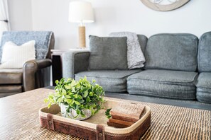 A living room with a grey sofa, a small side table with a lamp, and a coffee table with a plant and a woven tray. - Caddy's Boat House – Waterfront Balcony, Pet-Friendly & Steps from Indian Shores Beach (Indian Shores)