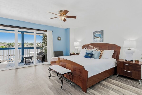 A bedroom with a bed, bedside tables, a ceiling fan, and a view of the outdoors.