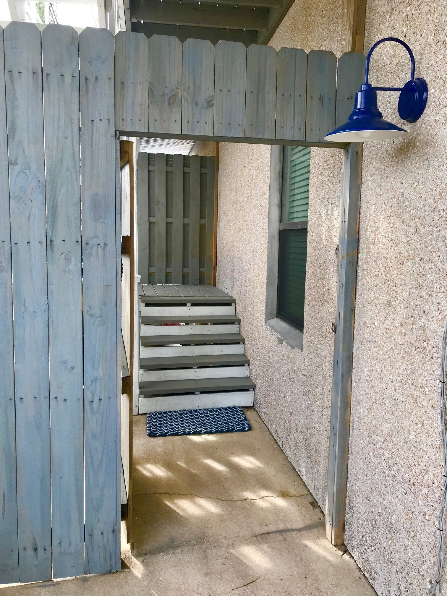 A wooden deck with a metal railing, a concrete pathway, and a blue outdoor light fixture.