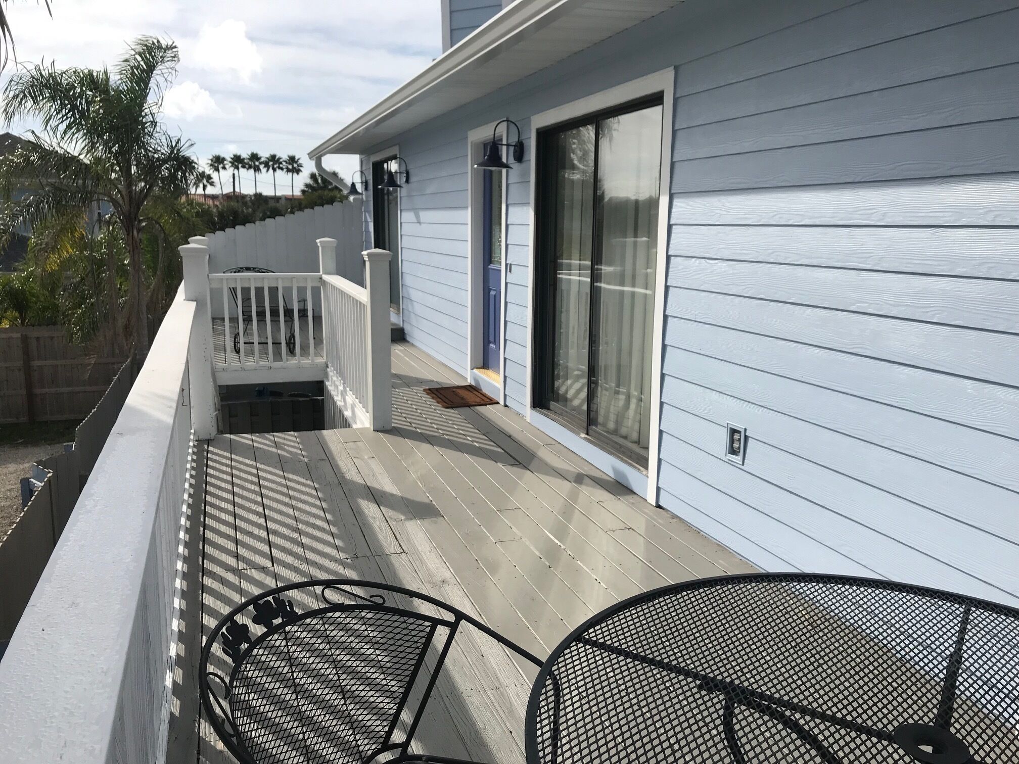 A covered deck with a white railing, a sliding glass door, and two metal chairs.
