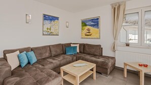 Uma sala de estar com um sofá seccional marrom, uma mesa de centro de madeira e duas pinturas na parede.