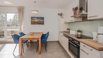 A modern kitchen with a wooden table and blue chairs, a built-in oven, and a view of the outdoors.