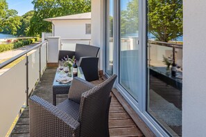 Ein Balkon mit Tisch für zwei Personen, Korbstühle und Blick auf einen See.