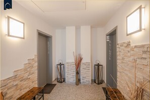 A reception area with a stone wall, two doors labeled "Banshin" and "Ahlbeck," and a central vase with dried plants. - Cozy vacation apartment in Korswandt on the lake with balcony and lake view (Korswandt)