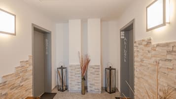 A reception area with a stone wall, two doors labeled "Banshin" and "Ahlbeck," and a central vase with dried plants.