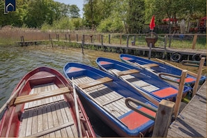 Una fila de barcos de madera amarrados en un muelle con un pasillo de madera y una sombrilla roja al fondo.