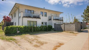 Uma casa moderna de dois andares, com varanda, calçada de acesso pavimentada e muro de tijolos.