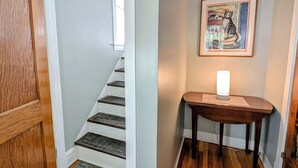 A staircase with wooden steps and a white wall. There is a framed picture on the wall and a table with a lamp. - The Avondale Attic (Chicago)