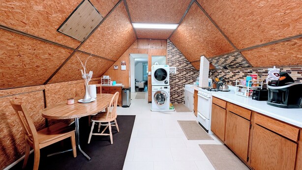 A compact kitchen with wooden cabinetry, a dining area with a table and chairs, and a washing machine. - The Avondale Attic (Chicago)