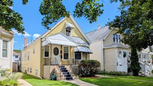 A two-story house with a front porch, a small front yard, and a visible staircase leading to the entrance. - The Avondale Attic (Chicago)