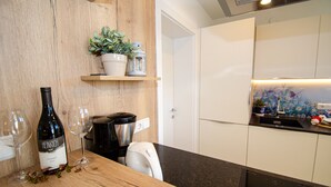 A modern kitchen with a wooden wall, a coffee machine, a wine bottle, and a potted plant on a shelf. - Apartment Nature & Friends - near Kaprun (Piesendorf)