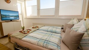 A bedroom with a bed, a television on a stand, a window, and a clock on the wall. - Apartment Nature & Friends - near Kaprun (Piesendorf)