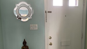 A door with a chain lock, a small table with a Buddha statue, and a wall-mounted mirror. - Beachside Townhouse: <br>Family Friendly & Renovated (Indian Harbour Beach)