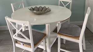 A dining area with a round table, four white chairs, and a decorative sign on the wall. - Beachside Townhouse: <br>Family Friendly & Renovated (Indian Harbour Beach)