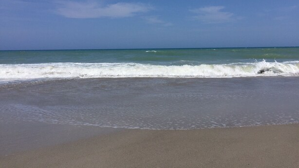 A beach with waves approaching the shore under a clear sky. - Beachside Townhouse: <br>Family Friendly & Renovated (Indian Harbour Beach)