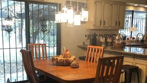 Un comedor con una mesa y sillas de madera, una lámpara colgante y vistas a través de amplios ventanales.