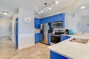A modern kitchen with blue cabinets, stainless steel appliances, and a white clock on the wall.