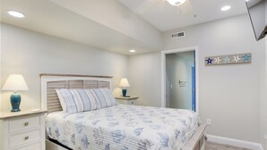 A bedroom with a bed, two bedside tables with lamps, a wooden bench, a door, and a wall with star decorations. - Love at First Flight: Oceanfront, Shared Pool (Kill Devil Hills)