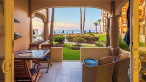 An open patio with a view of the ocean, a dining area with a table and chairs, and a seating area with a wicker sofa. - Surf & Stay; Beachfront Condo Steps from Sand - Heated Hot tub -Pool-Pickleball (San José del Cabo)
