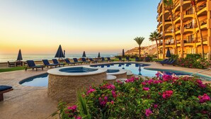 A resort pool area with lounge chairs and umbrellas, a hot tub, and a view of the ocean. - Surf & Stay; Beachfront Condo Steps from Sand - Heated Hot tub -Pool-Pickleball (San José del Cabo)